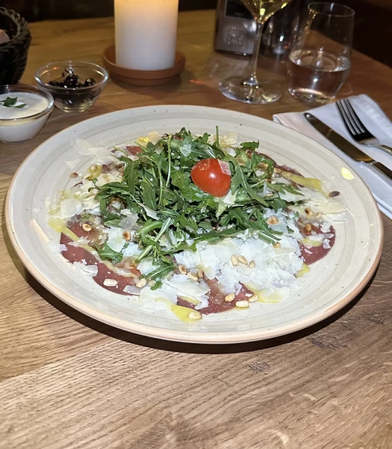 Hauchdünn geschnittenes Rinder Carpaccio mit Parmesan, Rucola und Pinienkernen, serviert im Trattoria Zollhof Düsseldorf Medienhafen.